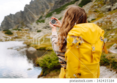 Person with backpack stands on rocky path in mountainous area while taking picture of waterfall. Person with backpack stands on rocky path in mountainous area while taking picture of waterfall. 142415184