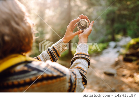 A person stands on a forest path holding a compass. The scene shows nature and adventure. A person stands on a forest path holding a compass. The scene shows nature and adventure. 142415197
