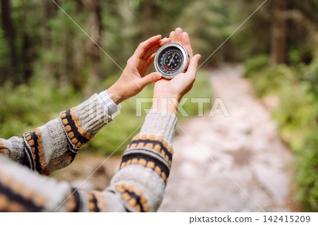 A person stands on a forest path holding a compass. The scene shows nature and adventure. A person stands on a forest path holding a compass. The scene shows nature and adventure. 142415209