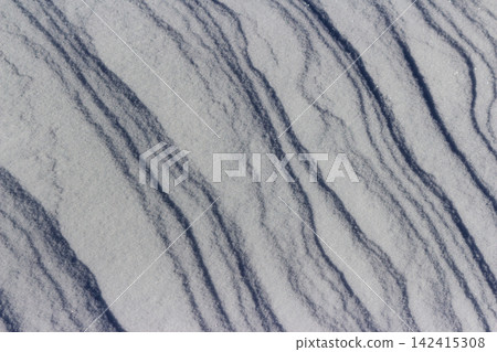 Sunlight glints off windblown snow patterns, creating crisp icy ripples and rhythmic shadows across a frozen field on a bright, cold winter morning with high contrast texture details Sunlight glints off windblown snow patterns, creating crisp icy ripples and rhythmic shadows across a frozen field on a bright, cold winter morning with high contrast texture details 142415308
