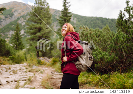 Woman hiking along a rocky trail surrounded by trees on a sunny day in the mountains 142415319