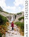 Woman hiking along a rocky trail surrounded by trees on a sunny day in the mountains 142415320