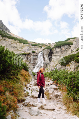 Woman hiking along a rocky trail surrounded by trees on a sunny day in the mountains Woman hiking along a rocky trail surrounded by trees on a sunny day in the mountains 142415320