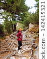 Woman hiking along a rocky trail surrounded by trees on a sunny day in the mountains 142415321