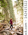 Woman hiking along a rocky trail surrounded by trees on a sunny day in the mountains 142415322