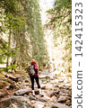 Woman hiking along a rocky trail surrounded by trees on a sunny day in the mountains 142415323