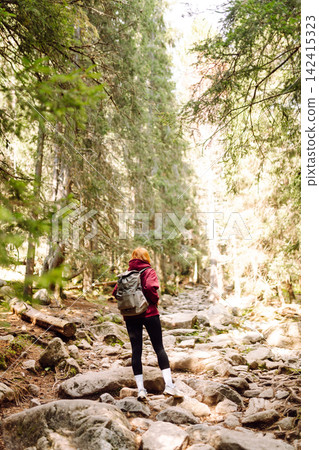 Woman hiking along a rocky trail surrounded by trees on a sunny day in the mountains 142415323