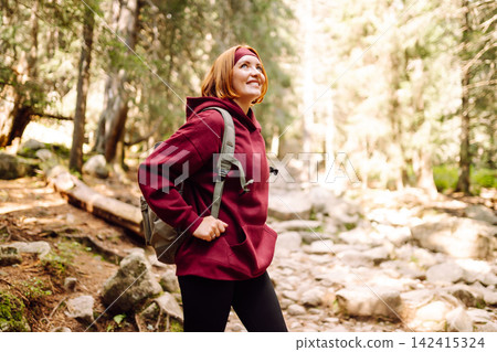 Woman hiking along a rocky trail surrounded by trees on a sunny day in the mountains 142415324