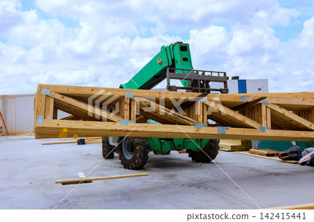 Telehandler forklift lifts heavy wooden beams at construction site workers are present nearby. Telehandler forklift lifts heavy wooden beams at construction site workers are present nearby. 142415441