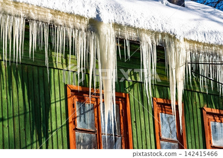 Bright winter sun illuminates sharp icicles adorning an old green wooden house, a visual reminder of cold days and potential heat loss from aging structures, Russia Bright winter sun illuminates sharp icicles adorning an old green wooden house, a visual reminder of cold days and potential heat loss from aging structures, Russia 142415466