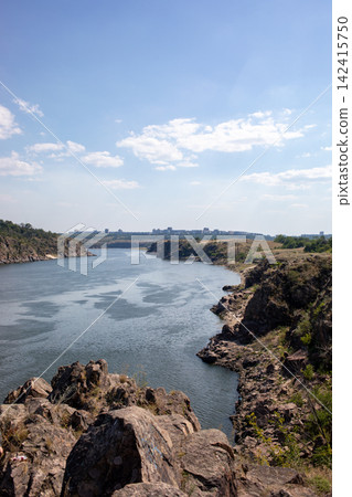 Vertical view of a scenic river winding between rugged rocky banks under a bright blue sky, capturing dramatic cliffs, calm water, wild summer nature and peaceful landscape scenery 142415750