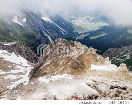 Dramatic alpine panorama from the Mindelheim Via Ferrata in the Allgaeu Alps, Germany, partially snow covered mountain slopes and rugged peaks emerging through clouds, cinematic adventure travel Dramatic alpine panorama from the Mindelheim Via Ferrata in the Allgaeu Alps, Germany, partially snow covered mountain slopes and rugged peaks emerging through clouds, cinematic adventure travel 142416404