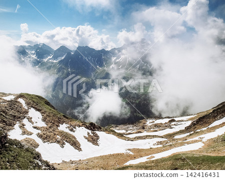 Dramatic alpine panorama from the Mindelheim Via Ferrata in the Allgaeu Alps, Germany, partially snow covered mountain slopes and rugged peaks emerging through clouds, cinematic adventure travel Dramatic alpine panorama from the Mindelheim Via Ferrata in the Allgaeu Alps, Germany, partially snow covered mountain slopes and rugged peaks emerging through clouds, cinematic adventure travel 142416431