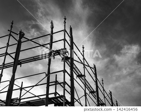 建築工地的鷹架和陰沉的天空:一幅單調、令人不安的經濟和商業畫面。 建築工地的鷹架和陰沉的天空:一幅單調、令人不安的經濟和商業畫面。 142416456