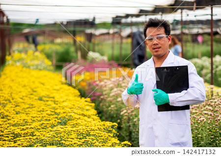 Researcher man giving thumbs up with clipboard in colorful flower nursery, confident positive expression representing science, horticulture, plant quality, success and professional approval Researcher man giving thumbs up with clipboard in colorful flower nursery, confident positive expression representing science, horticulture, plant quality, success and professional approval 142417132
