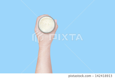 A hand holding a glass of milk against a blue background, top view. 142418913