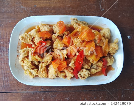 Sweet and sour chicken topped with fresh carrot slices in a centered close up top view 142419079
