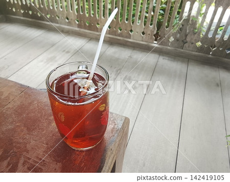 Iced sweet tea in a glass cup with straw on wooden table high angle shot Iced sweet tea in a glass cup with straw on wooden table high angle shot 142419105