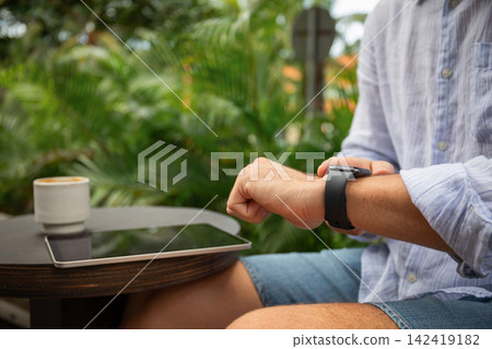 Freelancer using smartwatch and tablet at a tropical cafe 142419182