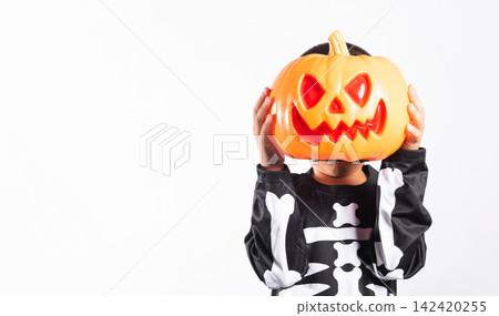 Halloween kid holding carved pumpkin bucket wearing skeleton costume celebrating holiday party against isolated white background with festive autumn spirit Halloween kid holding carved pumpkin bucket wearing skeleton costume celebrating holiday party against isolated white background with festive autumn spirit 142420255