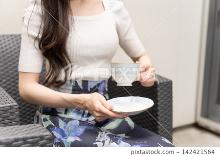 一位年輕女子手持咖啡杯站在露臺上。 一位年輕女子手持咖啡杯站在露臺上。 142421564