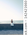 A young woman holding a film camera with the sea as a backdrop. 142421660