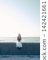 A young woman holding a film camera with the sea as a backdrop. 142421661