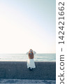 A young woman holding a film camera with the sea as a backdrop. 142421662