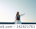 A young woman standing on the beach with a camera hanging from her shoulder. 142421761