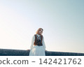 A young woman standing on the beach with a camera hanging from her shoulder. 142421762