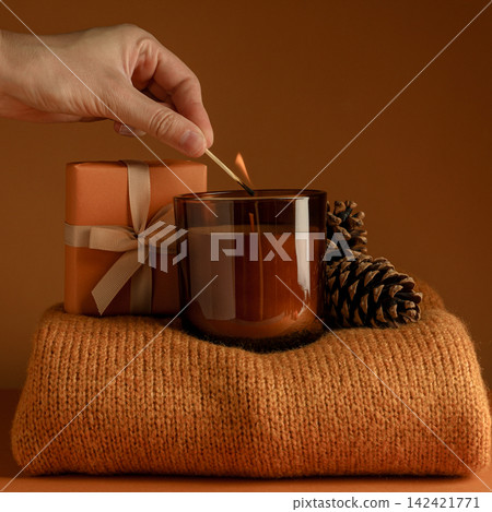 Candle, cones and gift on sweater, female hand on orange backgro Candle, cones and gift on sweater, female hand on orange backgro 142421771
