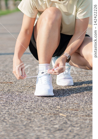 Young Asian woman tying running shoes in the park. Female runner getting ready for jogging and exercise on the road. Fitness, wellness and outdoor sport concept in morning Young Asian woman tying running shoes in the park. Female runner getting ready for jogging and exercise on the road. Fitness, wellness and outdoor sport concept in morning 142422226