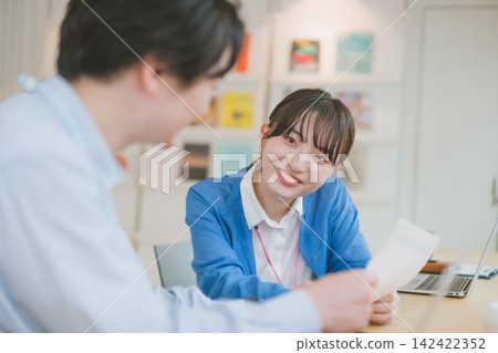 場景：一名女員工坐在辦公桌前，微笑地看著一名男員工。 142422352