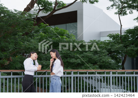 Asian businesswomen talking during coffee break outdoors for workplace stress relief Asian businesswomen talking during coffee break outdoors for workplace stress relief 142423464