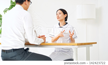 A woman in a white coat conducting a medical interview. Nurse, doctor, industrial physician, consultation, interview, examination, medical treatment, health checkup, reception, clinic, pharmacist A woman in a white coat conducting a medical interview. Nurse, doctor, industrial physician, consultation, interview, examination, medical treatment, health checkup, reception, clinic, pharmacist 142423722