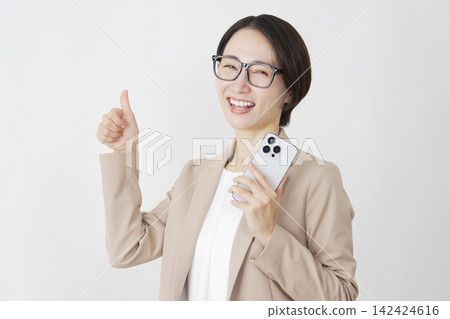 一位中年女商人在白色背景前舉起智慧型手機，豎起了大拇指。 142424616