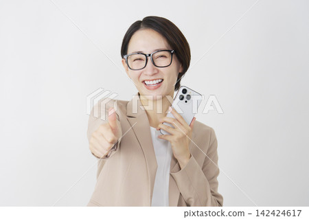 一位中年女商人在白色背景前舉起智慧型手機，豎起了大拇指。 142424617