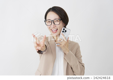 一位中年女商人在白色背景前舉起智慧型手機，比出和平手勢。 142424618