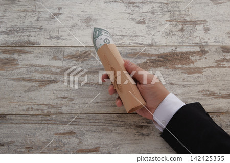 A hand in a business suit holding a gift wrap tied with string with a dollar bill peeking out on a wooden background A hand in a business suit holding a gift wrap tied with string with a dollar bill peeking out on a wooden background 142425355
