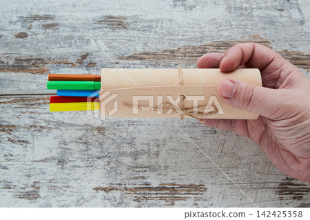 A hand holding a gift wrap with colorful markers on a wooden background. A hand holding a gift wrap with colorful markers on a wooden background. 142425358