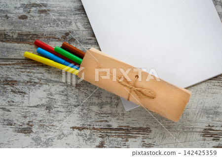 A gift wrap with colorful markers and a white sheet of paper lie on a wooden table. A gift wrap with colorful markers and a white sheet of paper lie on a wooden table. 142425359