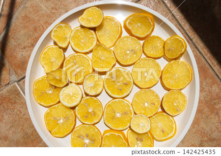 Fresh Lemon Slices Drying in the Sun on a White Plate Fresh Lemon Slices Drying in the Sun on a White Plate 142425435