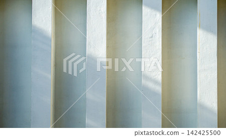 White concrete pillars wall with minimalist architecture pattern, natural sunlight shadow lines on cement surface, modern building texture background, and space interior design concept. White concrete pillars wall with minimalist architecture pattern, natural sunlight shadow lines on cement surface, modern building texture background, and space interior design concept. 142425500