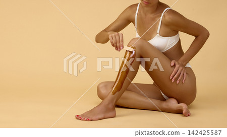 Woman spreads warm wax down shin during home epilation Woman spreads warm wax down shin during home epilation 142425587