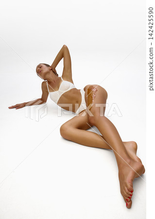 Woman poses in white lingerie with wax applied to leg 142425590