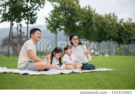 Asian family spending a quality time together on a picnic blanket mat over grass lawn in green park. Asian family spending a quality time together on a picnic blanket mat over grass lawn in green park. 142425663