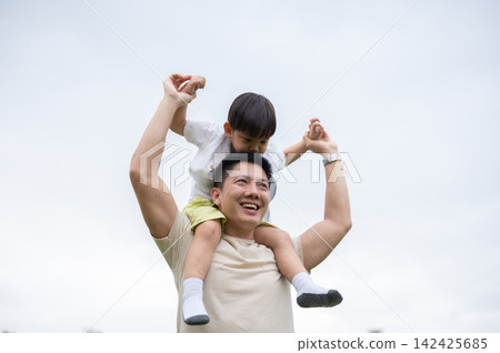 Asian father and son enjoy playful bonding together with shoulder ride while walking under clear sky 142425685