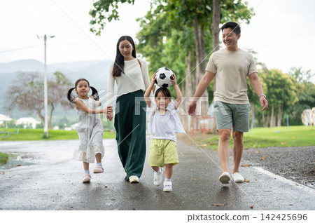 Asian parents and children walking together with soccer ball on park pathway during a family outing. Asian parents and children walking together with soccer ball on park pathway during a family outing. 142425696