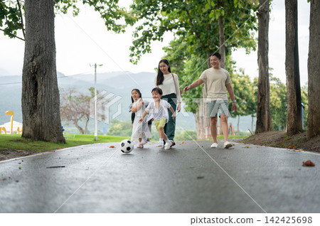 Asian parents walking while looking out for children playing a soccer ball on pathway in the park. Asian parents walking while looking out for children playing a soccer ball on pathway in the park. 142425698