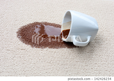 A white coffee mug creating a large brown stain on carpet. 142426234